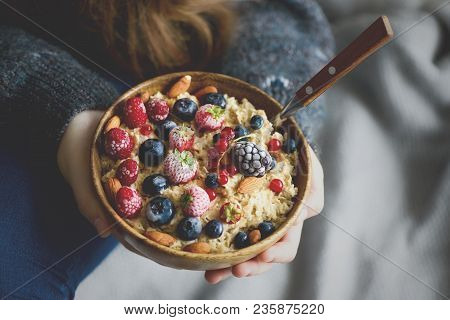 Girl Hands Holding Oatmeal Porridge With Frozen Berries, Almonds In Wooden Bowl. Healthy Breakfast. 