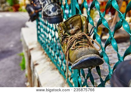 Old battered boot with lace rope used as decoration for shabby metal fence.