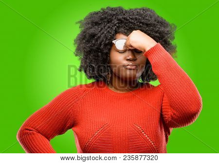 Beautiful african woman with sleepy expression, being overworked and tired, rubbes nose because of weariness