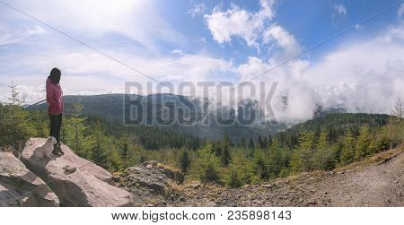 Young Brunette Woman Standing With Her Dog On A High Rock, Admiring The View Of The Mountains And Cl