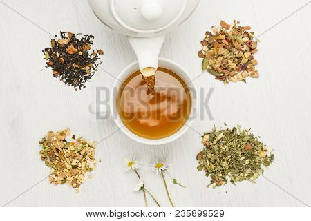 Pouring Tisane Into Cup With Variety Of Herbal Tea On Table