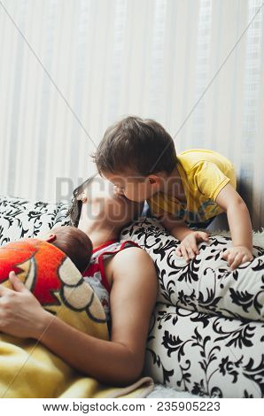 Mom Holds A Newborn Baby In Her Arms And Kisses Her Son, At Home In Comfort