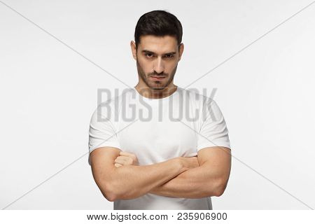 Serious Young Man Portrait. Tough Guy Standing With Crossed Arms Isolated On Grey Background