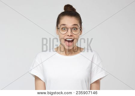 Indoor Shot Of Attractive Young Woman With Brown Hair Tied In Bun Isolated On Grey Background, Smili