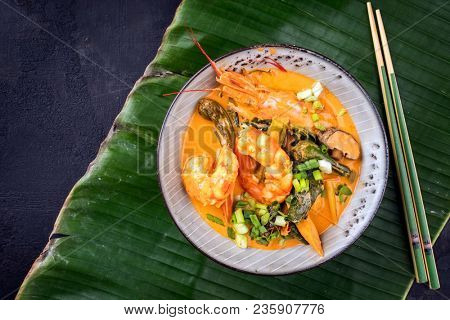 Traditional Thai kaeng phet red curry with king prawns and galgant as top view in a bowl on a banana leaf with copy space left 
