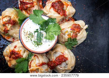 Traditional kazakh manti steamed with mincemeat garnished with yogurt and salca as top view on a board with copy space right