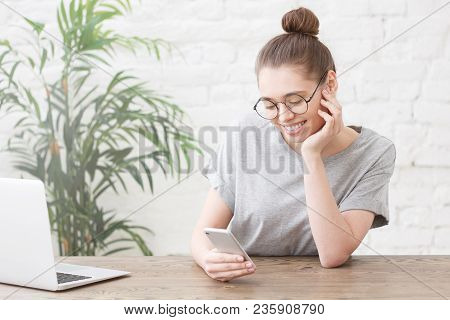 Smiling Young Female Entrepreneur Sitting At Wooden Table In Her White Lof Kitchen Writing Message W