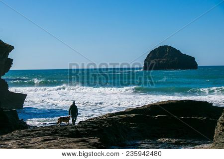 Dog Walker Owner And Her Pet Wait For The Tide To Retreat At The Sandy Beach Of Trebarwith Strand In