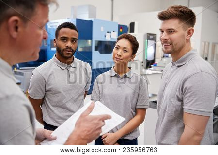 Engineering Team Meeting On Factory Floor Of Busy Workshop