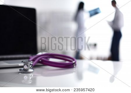 Laptop And Medical Stethoscope On The Desk , Doctors Standing In The Background.