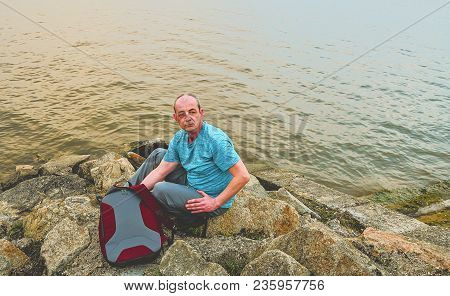 Midle Aged Man Sitting On The Shore Of The Lake. Solitude Mature Man Sitting On The Bank. Concept Of