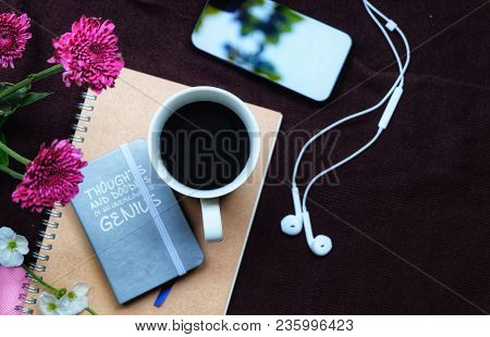 A Black Coffee With Notepad, Mobile Phone, Earplugs On A Dark Brown Background