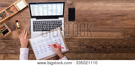 An Overhead View Of Businesswoman Marking Date On Calendar With Gantt Chart On Laptop Screen