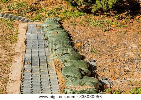 Small Green Sandbags On Ground Next To Water Runoff Culvert.