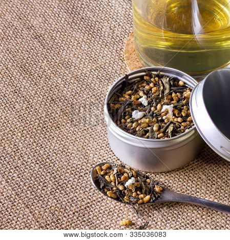 Organic And Natural Brown Rice Tea, Genmaicha In A Container. Accompanied By A Cup Of Hot Tea On Bro