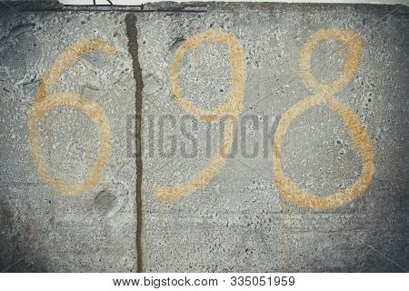Number 698 Yellow On A Textured Gray Concrete Wall With Scratches And Cracks.