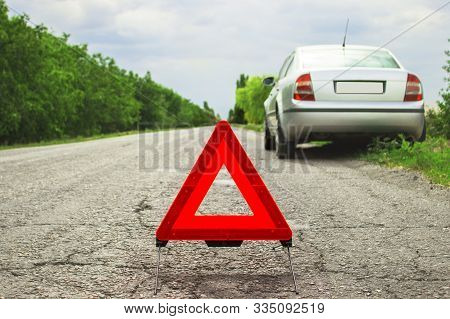 Red Triangle Of A Car On The Road. Car Warning Triangle On The Road Against The City In The Evening.