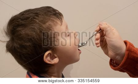 Small Kid Close Up Eating From The Spoon Which Is Holding By The Adult Hand. Sick Baby Eating Medici