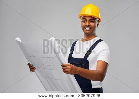 profession, construction and building - happy smiling indian builder in helmet with blueprint over grey background