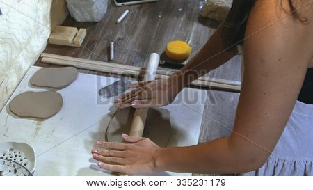 Top View Of A Woman Potter Wearing An Apron Preparing And Rolling Clay With A Rollingpin. Female Han