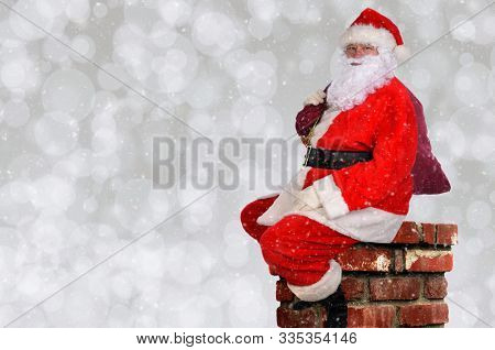 Santa Claus with his bag of toys sitting atop a chminey, with silver bokeh background and snow flake effect.