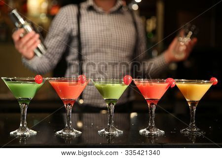 Multi-colored Cocktails Close-up. Barman With A Shaker And Five Different Cocktails On A Black Bar C