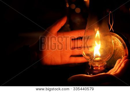 Human Hands Next To Litted Oil Lamp In A Gloom Dark Night