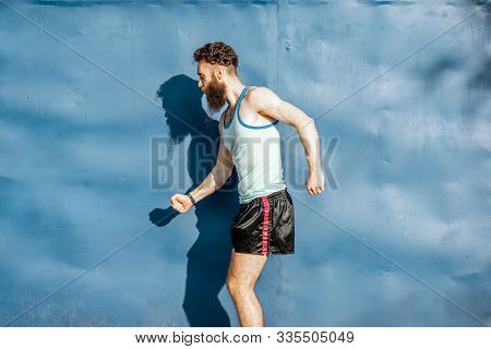 Funny Portrait Of An Old-fashioned Athlete Dressed In 80s Style Posing On The Blue Wall Background
