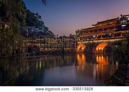 Illuminated At Night Old Historic Arched Bridge On The Riverbanks Of Tuo River, Flowing Through The 