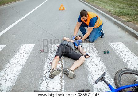 Road Accident With Injured Cyclist On The Pedestrian Crossing With Passerby Pedestrian Providing Fir