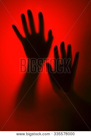 Silhouette of a female hand through glass on a red background. Horror concept