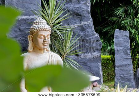 Face Shot Of A Buddha Statue With Green Leaves In The Foreground. Buddhism And Religion Concept