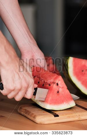 Hands Chop Watermelon With A Knife On A Bamboo Cutting Board. Side View