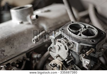 Engine Compartment Of An Old Car. Close-up View Of A Gasoline Carburetor Against A Background Of A C