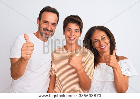 Family of three, mother, father and son standing over white isolated background doing happy thumbs up gesture with hand. Approving expression looking at the camera showing success.