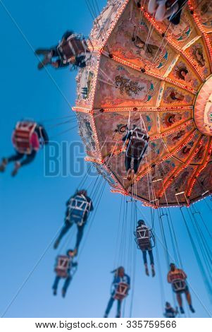 Amusement Park Motion Blurred Riders On Retro Vintage Tilting Swing Against Clear Blue Sky.