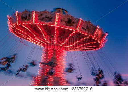 Amusement Park Motion Blurred Riders On Brightly Lit Retro Vintage Tilting Swing At Blue Hour.