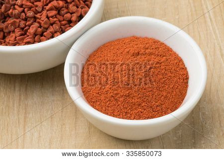 Bowl with dried whole Annatto seeds and a bowl with ground Annatto powder close up