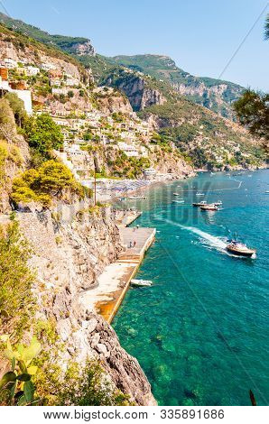 Amazing Positano Cityscape On Rocky Landscape, People On The Beach, Boats Are Coming And Going To Th