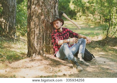 Woodcutter With Axe In The Summer Forest. Illegal Logging Continues Today. Lumberjack Standing With 
