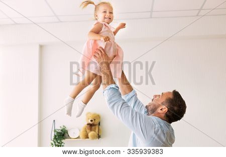 Happy Childhood. Joyful Father Tossing Up His Daughter, Throwing Little Girl Up In The Air