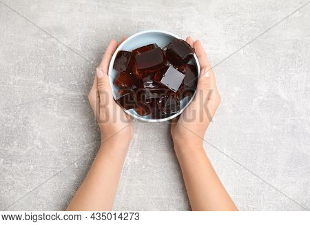 Woman Holding Bowl With Delicious Grass Jelly Cubes At Light Grey Table, Top View