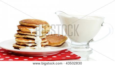 หวาน pancakes บนแผ่นกับนมข้นที่แยกต่างหากบนพื้นสีขาว