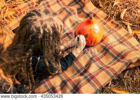 Halloween. Cute Girl Draws A Funny Face To A Pumpkin.