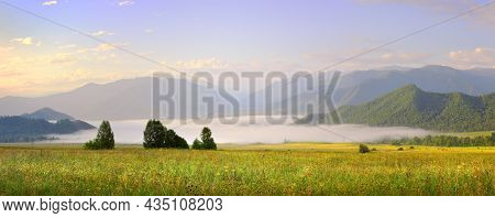 Fog Over A Green Meadow Against The Background Of Blue Mountains Under The Morning Sky. Siberia, Rus