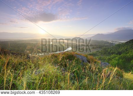 A Blooming Mountain Slope Above The Katun Valley, The Sun Above The Horizon Under A Golden-blue Sky 