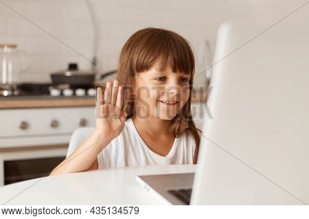 Portrait Of Cute Dark Haired Female Child Sitting At Table Having Video Call, Looking At Laptop Disp
