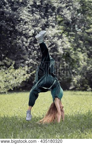 Woman In Emerald Clothing Makes A Flip On Her Arms In The Park On The Lawn