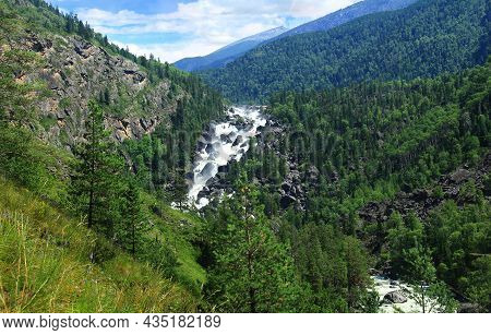 The Fast Uchar River In Altai, High In The Mountains In The Gorge, Flows Over Huge Rocks, The Mounta