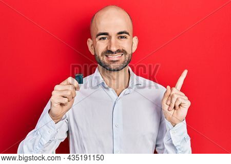 Young bald man holding sdxc card smiling happy pointing with hand and finger to the side 